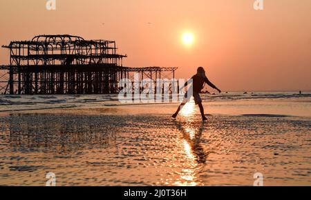 Brighton UK 20. March 2022 - Eine junge Frau tanzt bei Ebbe auf dem Sand, während die Sonne am Brighton Beach während des Frühlings-Tagundnachtgleiche untergeht, da das warme, sonnige Wetter in ganz Großbritannien in der nächsten Woche anhalten wird : Credit Simon Dack / Alamy Live News Stockfoto