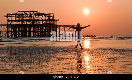Brighton UK 20. March 2022 - Eine junge Frau tanzt bei Ebbe auf dem Sand, während die Sonne am Brighton Beach während des Frühlings-Tagundnachtgleiche untergeht, da das warme, sonnige Wetter in ganz Großbritannien in der nächsten Woche anhalten wird : Credit Simon Dack / Alamy Live News Stockfoto