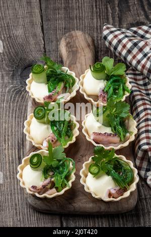 Minitörtchen gefüllt mit mariniertem Tintenfisch und Muscheln auf einem Holztisch Stockfoto