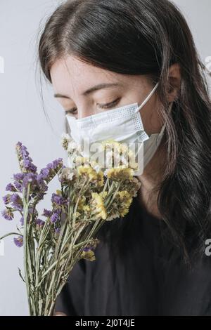 Junge Frau in schützende medizinische Maske schnüffelt gelbe Blume Stockfoto