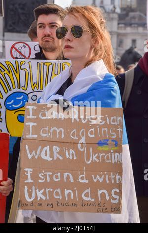 London, Großbritannien. 20.. März 2022. . Ein russischer Protestler, der in die symbolische blau-weiße russische Flagge gehüllt ist und die rote Farbe entfernt hat, hält ein Antikriegszeichen. Auf dem Trafalgar-Platz versammeln sich weiterhin große Menschenmengen zur Unterstützung der Ukraine, während Russland seinen Angriff verstärkt. Kredit: Vuk Valcic/Alamy Live Nachrichten Stockfoto