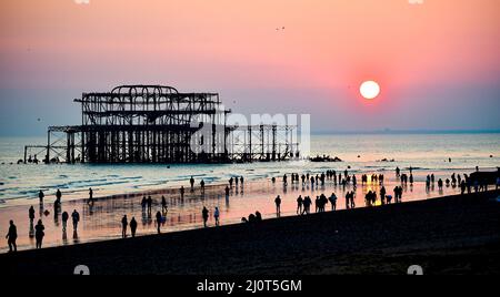 Brighton UK 20. March 2022 - Menschenmassen beobachten den Sonnenuntergang hinter Brighton's West Pier am Frühlings-Tagundnachtgleiche, da sich das warme, sonnige Wetter in ganz Großbritannien in der nächsten Woche fortsetzen wird : Credit Simon Dack / Alamy Live News Stockfoto