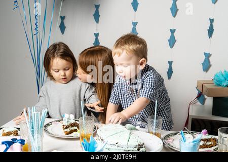 Brüder. Knabengeburtstag am Tisch. Die Jungs am Tisch schneiden einen Geburtstagskuchen. Stockfoto