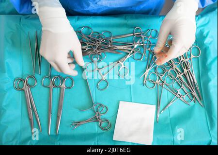 Mehrere Operationsinstrumente auf blauem Tisch über der Ansicht. Chirurg nehmen chirurgische Werkzeuge vom Tisch. Stockfoto