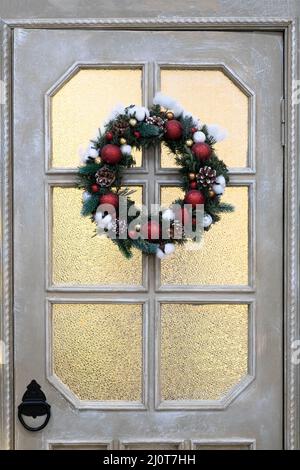 Weihnachtskranz, eine Weihnachtsdekoration mit einem Ornament aus roten Kugeln an einer Holztür zum Aufhängen. Stockfoto