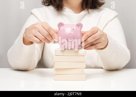 Pinkfarbenes Sparschwein aus Keramik und Holzklötze. Konzept der Erhöhung des Zinses auf eine Einzahlung in einer Bank, hohe Rendite auf Investitionen, lar Stockfoto