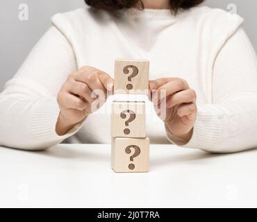 Weibliche Hand mit einem Holzwürfel mit Fragezeichen, Konzept der Antworten und Fragen, Spannung und Lösungsmethoden, schließen U Stockfoto