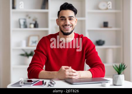 Porträt Eines Lächelnden, Gut Aussehenden Arabischen Mannes, Der Im Home Office Am Schreibtisch Sitzt Stockfoto
