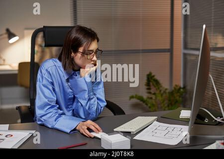 Seitenansicht Porträt einer müden jungen Geschäftsfrau, die am Arbeitsplatz einen Computer benutzt und spät in der Nacht im Büro arbeitet Stockfoto