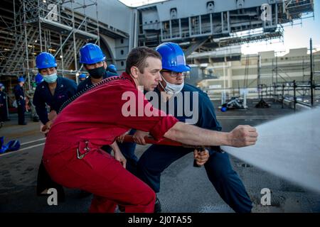 Damage Controlman 2. Class Chase Purdue, links, gibt Seeleuten an Bord des Flugzeugträgers USS George H. W. Bush (CVN 77) Anweisungen zur Schlauchhandhabung. GHWB befindet sich derzeit in der Norfolk Naval Shipyard wegen der geplanten Andockbarkeit. (USA Navy Foto von Mass Communication Specialist 3. Class Brandon Roberson) Stockfoto