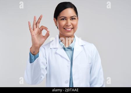 Alles ist perfekt. Beschnittenes Porträt einer attraktiven jungen Wissenschaftlerin, die im Studio vor grauem Hintergrund a-okay gestikuliert. Stockfoto