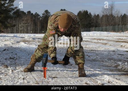 ÄSCHEN, mich. – Stabsmitarbeiter der US-Armee Joshua McKee, ein nicht beauftragter Offizier der Brandbekämpfung bei Bravo Battery, Bataillon 1., Artillerieregiment 182., Michigan National Guard, hämmert einen Pfahl in den Boden, um einen nahezu vertikalen Skywave-Satelliten zu sichern, der während der Teilnahme am Northern Strike 22-1 am 21. Januar 2022 für Kommunikation sorgt. Northern Strike 22-1 („Winterstreik“) ist eine vom National Guard Bureau gesponserte Übung, die Dienstmitglieder aus mehreren US-Bundesstaaten und Partnereinheiten vom 21. Bis 30. Januar 2022 im Camp Greyling Joint Maneuver Training Center und im Alpena Comb vereint Stockfoto