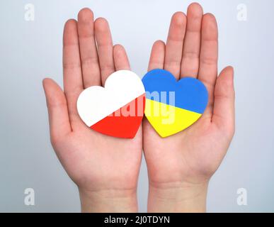 Zwei Herzen mit Fahnen polens und der ukraine in Händen auf grauem Hintergrund. Einheitensolidarität Hilfskonzept Stockfoto