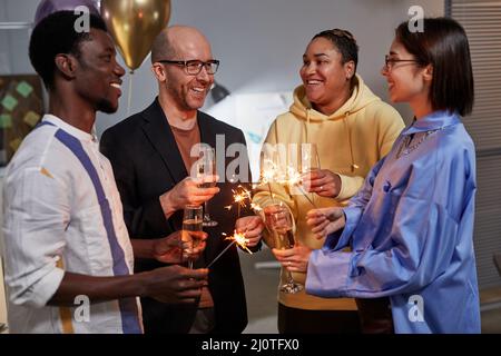 Porträt einer Gruppe von Kollegen, die Champagner genießen und Wunderkerzen beim Feiern im Büro beleuchten Stockfoto