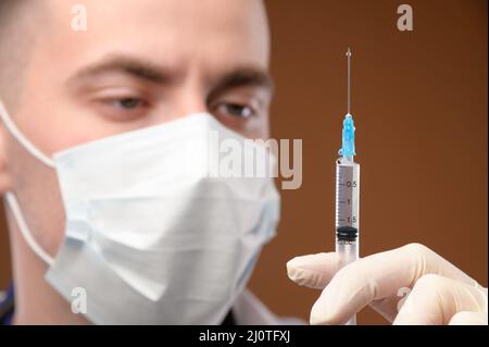 Nahaufnahme eines kaukasischen Arztes, der eine Spritze für die Injektion vorbereitet. Junger Arzt in einer Schutzmaske und Handschuhen halten Stockfoto