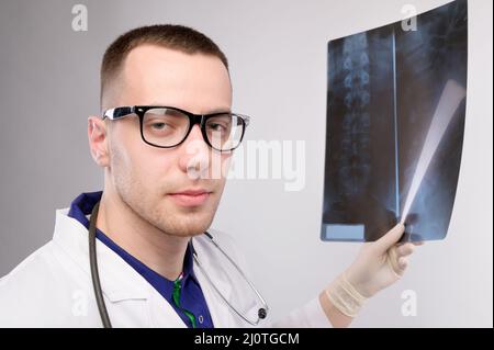 Der junge kaukasische Radiologe hält ein Röntgenbild in der Hand und blickt in die Kamera. Ein Mann in Brille und Uniform Stockfoto