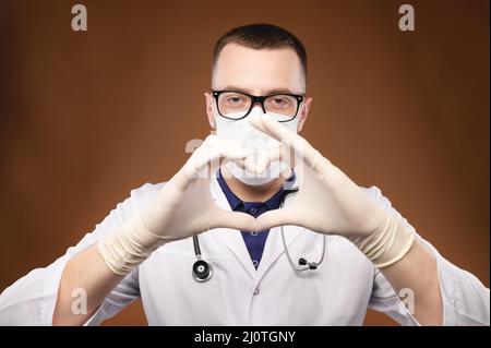 Porträt eines jungen männlichen Arztes in einer Brille, die die Herzgeste im Studio auf grauem Hintergrund hält Stockfoto