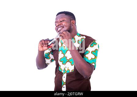 Ein hübscher junger Geschäftsmann in Lendenschurzhemd, der auf weißem Hintergrund steht und versucht, sich seinen Bart zu schneiden, lächelnd. Stockfoto