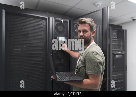 Rechenzentrumsingenieur, der die Einrichtung eines Spezialisten für Laptop-Computer im Serverraum verwendet, mit einem männlichen Systemadministrator, der mit Data Prot zusammenarbeitet Stockfoto