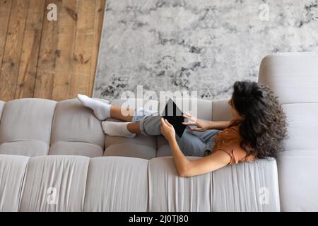 Draufsicht auf junge Frau mit Tablet-Computer auf dem Sofa sitzen, online arbeiten oder von zu Hause aus studieren, Mockup für App Stockfoto