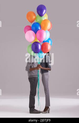 Kleben hinter Ballons. Studioaufnahme eines Paares, das sich hinter einem Haufen Ballons versteckt. Stockfoto