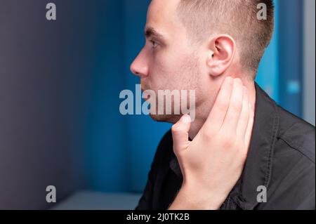 Nahaufnahme eines Mannes, der seinen Hals mit der Hand hält. Nackenschmerzen und Selbstmassage Stockfoto