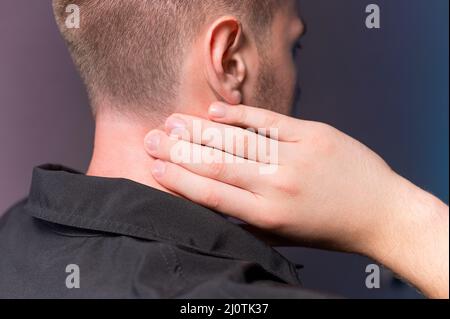 Nahaufnahme eines Mannes, der seinen Hals mit der Hand hält. Nackenschmerzen und Selbstmassage Stockfoto