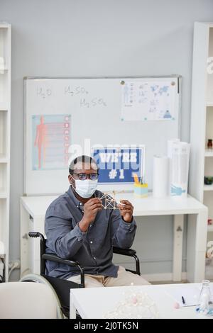 Vertikales Porträt eines afroamerikanischen Lehrers mit Maske und Molekülmodell während des Chemieunterrichtete in der Schule Stockfoto