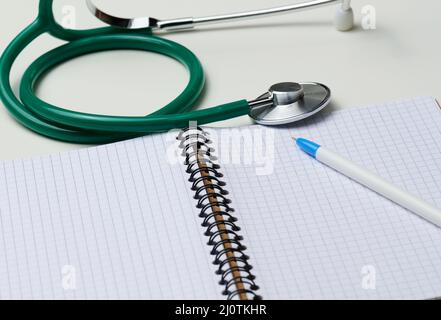 Offenes leeres Notizbuch mit Stift und Stethoskop, weißer Tisch Stockfoto