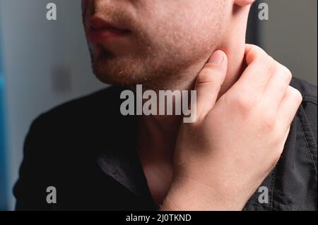 Nahaufnahme eines Mannes, der seinen Hals mit der Hand hält. Nackenschmerzen und Selbstmassage Stockfoto