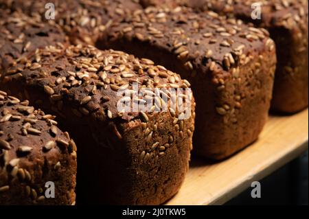 Frische braune Brote des Roggenbrotes in Form von Ziegel mit den Sonnenblumenkernen auf der Kruste. Legen Sie sich auf ein Holzgestell Stockfoto