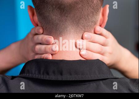 Nahaufnahme eines Mannes, der seinen Hals mit den Händen hält. Nackenschmerzen und Selbstmassage Stockfoto