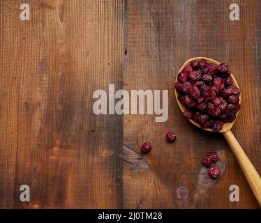 Ein paar getrocknete Preiselbeeren in einem Holzlöffel auf einem braunen Tisch. Köstliche Beeren, Blick von oben Stockfoto