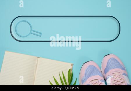 Ein Paar pinkfarbene Sneakers und ein offenes Notebook auf blauem Hintergrund, Sport. Speicherplatz kopieren Stockfoto