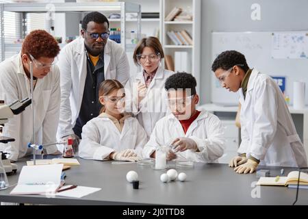 Eine vielfältige Gruppe von Kindern, die im Chemieunterricht Laborkittel tragen, während sie wissenschaftliche Experimente genießen Stockfoto