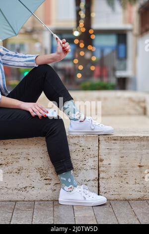 Unkenntliche Frau in lustigen Socken, die im Regen sitzt Stockfoto