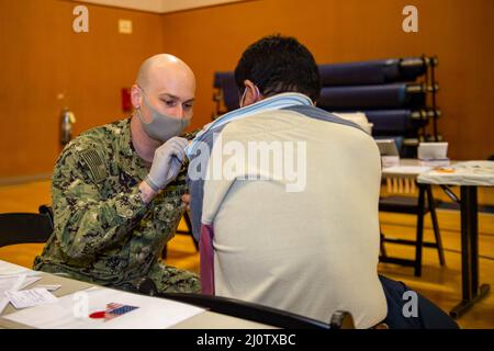 220128-N-SI601-1070 YOKOSUKA, Japan (Jan 28, 2022) Hospital Corpsman 2. Class Andrew Quigley aus Wichita, Kansas, der dem vorbereitenden Flugzeugträger der US-Marine USS Ronald Reagan (CVN 76) zugewiesen wurde, verwaltet einen COVID-19-Impfverstärker an einen japanischen Basismitarbeiter auf Commander, Fleet Activities Yokosuka. Ronald Reagan, das Flaggschiff der Carrier Strike Group 5, stellt eine kampfbereite Kraft zur Verfügung, die die Vereinigten Staaten schützt und verteidigt und Allianzen, Partnerschaften und kollektive maritime Interessen in der Indo-Pazifik-Region unterstützt. (USA Navy Foto von Mass Communication Specialist 3 Stockfoto