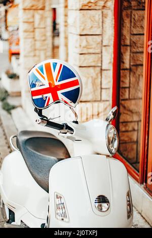 In der Nähe eines Steingebäudes steht ein weißer Roller mit Helm in den Farben der britischen Flagge Stockfoto