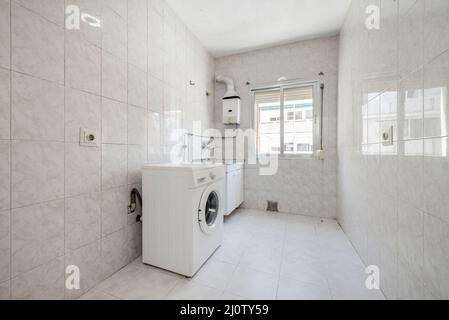 Zimmer mit Waschmaschine und Edelstahlwaschbecken mit Steinzeugböden und passenden Wänden Stockfoto