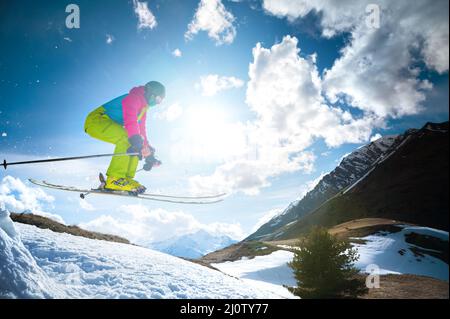 Mädchen Skifahrerin im Flug, nachdem sie im Frühling von einem Kicker vor dem Hintergrund von Bergen und blauem Himmel gesprungen war. Nahaufnahme weit Stockfoto