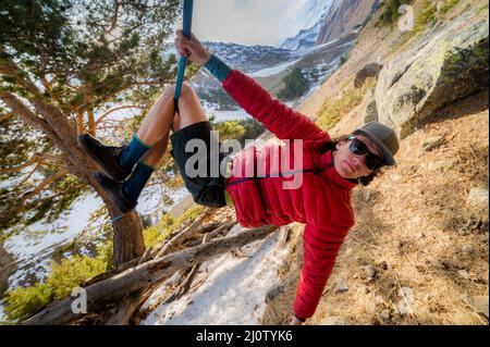 An einem sonnigen Tag hängt nachmittags ein Mann-Seiltänzer in einer Mütze und Sonnenbrille an einer Slackline. Das Konzept der Slackline re Stockfoto