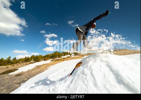 Stilvolle junge Mädchen Snowboarder tut den Trick in Springen aus einem Schneekicker gegen den blauen Himmel Wolken und Berge in der spr Stockfoto