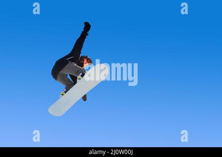 Snowboardermädchen macht einen Trick beim Springen mit einem Griff gegen den blauen Himmel. Blauer Hintergrund isoliert Athlet im Flug Stockfoto