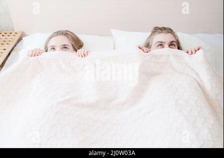 Ein junges Paar im Bett bedeckt die Hälfte ihrer Gesichter mit einer Decke, die sich hinter einer Decke versteckt. Das Konzept der familienfreien p Stockfoto