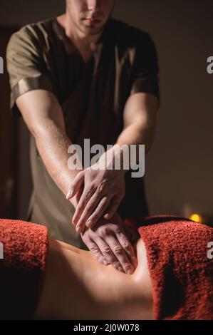 Professionelle Massage des Rückens und des unteren Rückens. Männlicher Masseur massiert eine Kundin in einem dunklen Raum bei Kerzenlicht an eine Frau Stockfoto