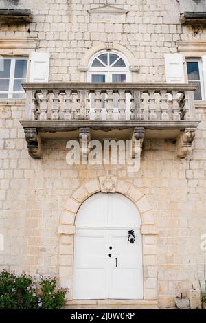 Steinbalkon auf einer Ziegelfassade eines alten Gebäudes mit einer gewölbten weißen Holztür Stockfoto