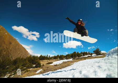 Stilvolle junge Mädchen Snowboarder tut den Trick in Springen aus einem Schneekicker gegen den blauen Himmel Wolken und Berge in der spr Stockfoto