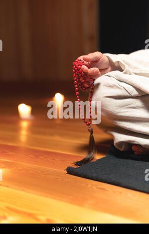 Nahaufnahme Mann in Kleidung für Praxis und Meditation sitzt in einer Lotushaltung und hält roten Rosenkranz, um die Aufmerksamkeit in einem Wald zu konzentrieren Stockfoto