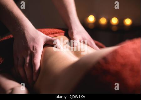 Professionelle Massage des Rückens und des unteren Rückens. Männlicher Masseur massiert eine Kundin in einem dunklen Raum bei Kerzenlicht an eine Frau Stockfoto