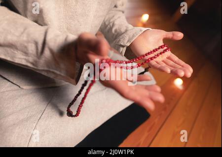 Nahaufnahme Mann in Kleidung für Praxis und Meditation sitzt in einer Lotushaltung und hält roten Rosenkranz, um die Aufmerksamkeit in einem Wald zu konzentrieren Stockfoto